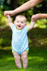 Happy baby boy learning to walk on grass outdoors